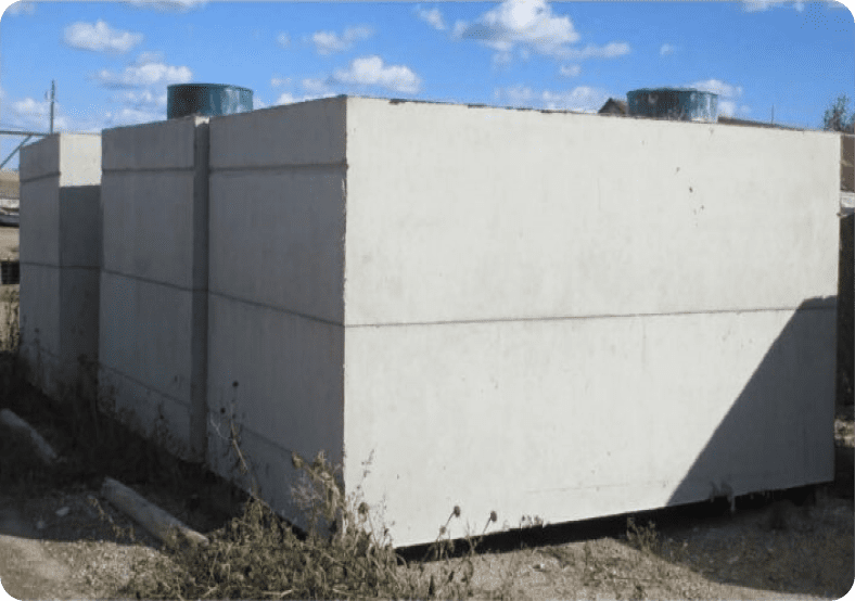 Large rectangular concrete structure outdoors, featuring two cylindrical vents on top and surrounded by sparse vegetation under a partly cloudy sky.